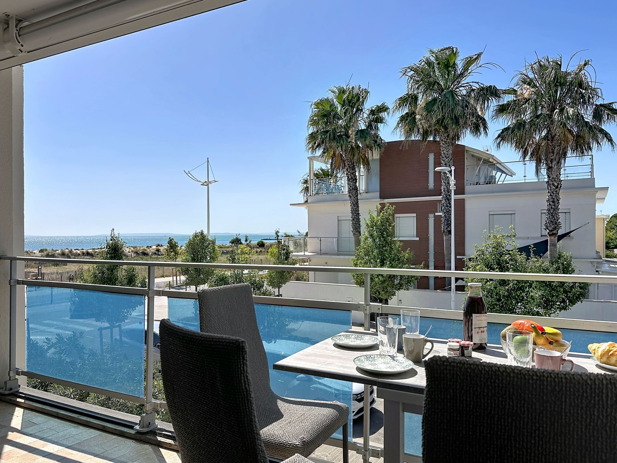 A balcony with a view of the sea, a table with plates and a bottle, and chairs.