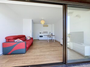 Un salon moderne avec un canapé rouge, une table à manger et, au fond, un coin cuisine.