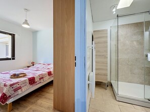 Ein Schlafzimmer mit Bett, Nachttisch, Fenster und einer Duschkabine mit Glastür.