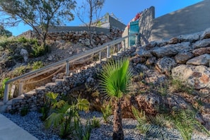 A stone staircase leading up to a building with a blue door, surrounded by rocks and greenery. - AER - Romantic Private Pool Villa with Spectacular 180° Ocean Views (Korissia)