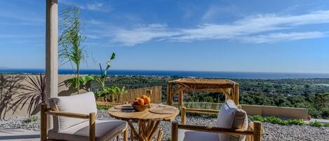 A patio with wicker furniture, a round table, and a view of the sea.