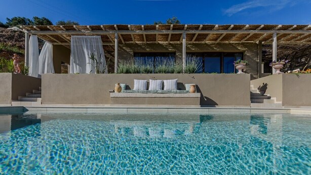 A swimming pool with a clear blue surface, a covered seating area with cushions, and a stone statue. - Romantic Private Pool Villa with Spectacular 180° Ocean Views (Korissia)