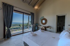 Een slaapkamer met een groot bed, uitzicht op het landschap, een kaptafel met spiegel en een deur naar een andere kamer.