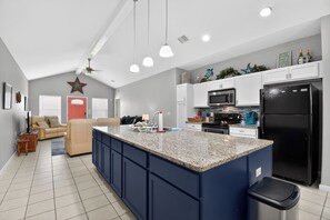 Una cocina moderna con una isla central, electrodomésticos integrados y un rincón comedor con sofá y mesa de centro.