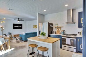Eine moderne Küche mit Kochinsel, ein Essbereich mit einer Couch und ein Wohnzimmer mit blauem Sofa und Deckenventilator.