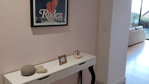 Quarto com uma mesa de consola branca encostada a uma parede rosa, um quadro emoldurado em cima e vista para uma varanda.