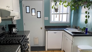 A kitchen with wooden flooring, white cabinets, a stove, a dishwasher, and a window with blinds. - Perfect 1-bedroom house in welcoming Ontonagon for a relaxing stay (Ontonagon)