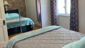 A bedroom with a bed, a mirror, a window with curtains, and a door. - Perfect 1-bedroom house in welcoming Ontonagon for a relaxing stay (Ontonagon)