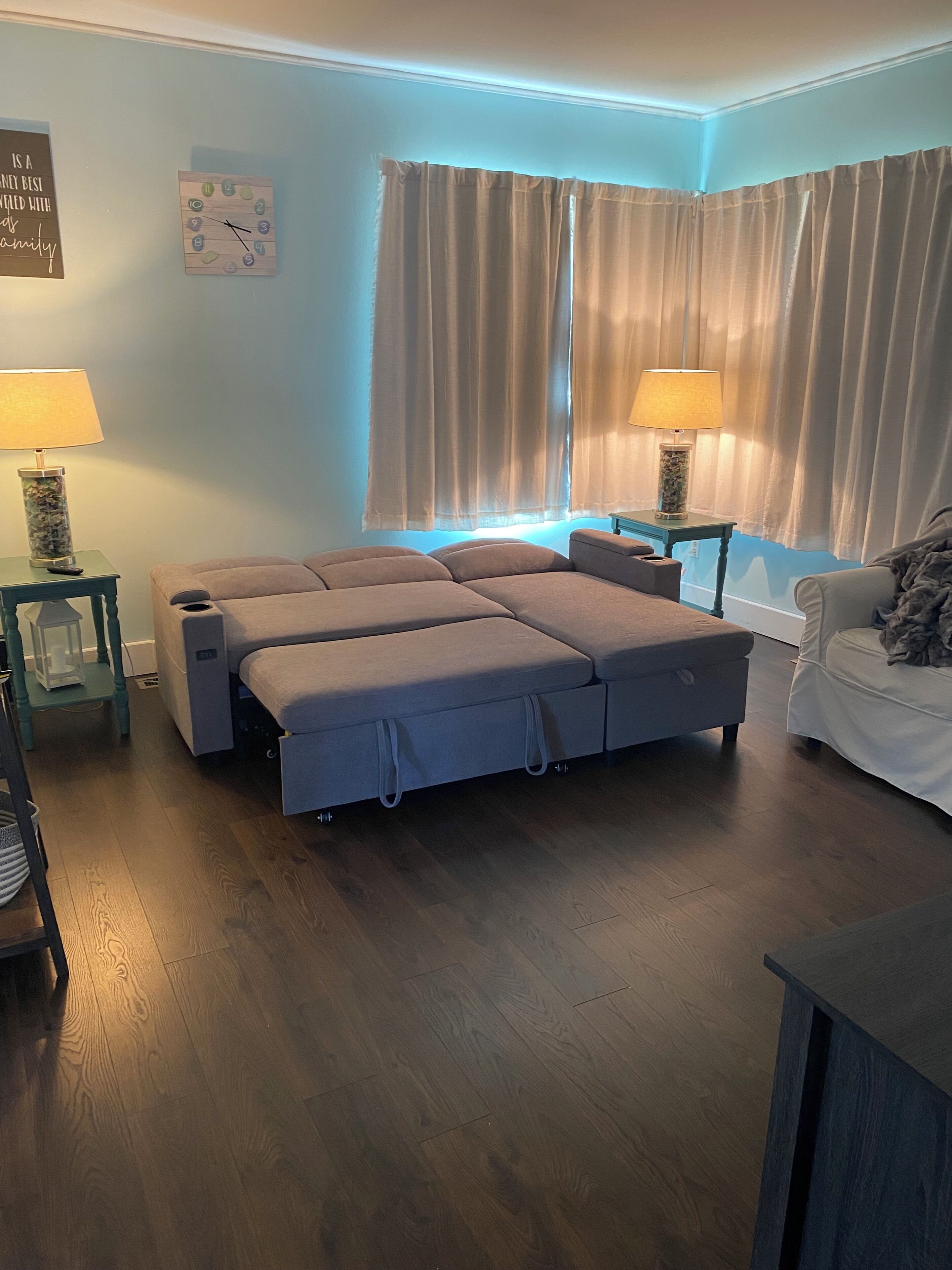 A room with a large bed, two bedside tables, a lamp, a chair, and a window with curtains.