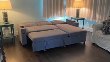 A room with a large bed, two bedside tables, a lamp, a chair, and a window with curtains.