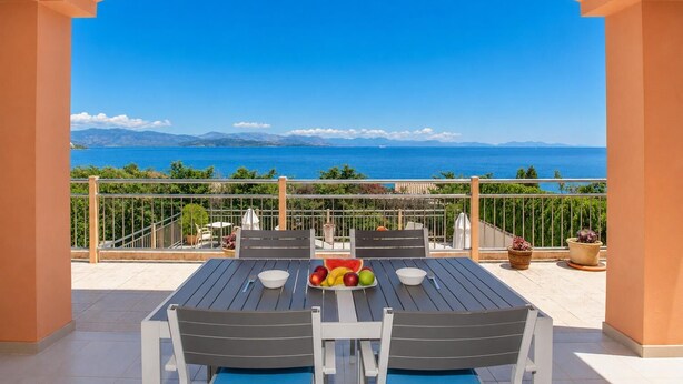 Eine Terrasse mit Tisch für zwei Personen, Blick aufs Meer und eine bergige Landschaft im Hintergrund.