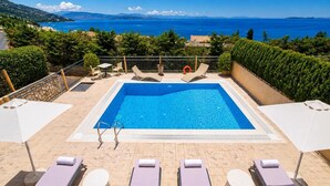 Ein rechteckiger Pool mit Meerblick, umgeben von Liegestühlen und einer Brüstung.