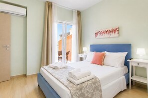 A hotel room with a bed, a nightstand, a lamp, a painting, and a sliding glass door to the outside.