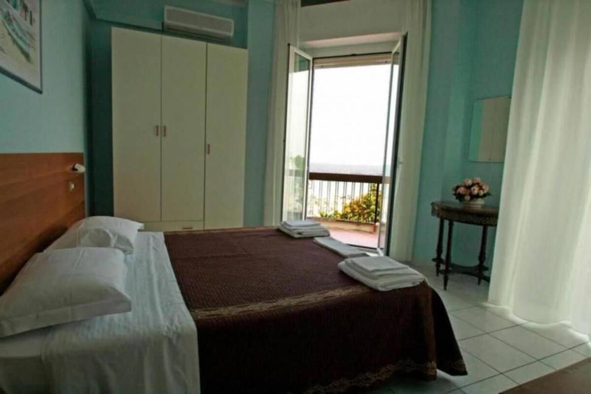 A hotel room with a bed, a wardrobe, a balcony with a view, and a small table with flowers.