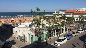 Uma área costeira com praia, carros estacionados e edifícios com placas visíveis.
