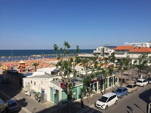 A coastal area with a beach, parked cars, and buildings with visible signage. - Hotel Acapulco (Rimini)