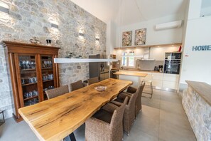Eine moderne Küche mit Steinwand, einem Holzespeisetisch, Weidekorbstühlen und einem eingebauten Schrank mit Gläsern.