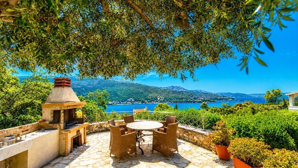 An outdoor patio with stone flooring, a round table with chairs, a brick oven, and potted plants. - Villa Apanemia - Three Bedroom Villa, Sleeps 6 (Kassiopi)