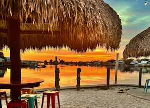 Blick auf einen Strand mit einem Reetdachschirm, einem Holztisch und einem Stuhl.