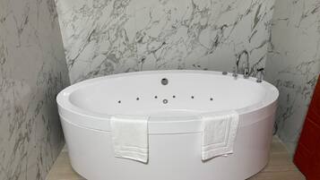 Un bagno moderno con una grande vasca da bagno ovale, pareti in marmo e una parete di accento rossa.