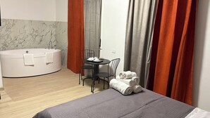 Et moderne hotelværelse med en stor seng, et rundt badekar, et lille bord med stole samt et skrivebord med tilhørende stol.
