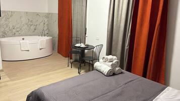 Una camera d'albergo moderna con un letto grande, una vasca da bagno rotonda, un tavolino con sedie e una scrivania con sedia.
