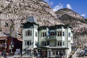 Ein mehrstöckiges Gebäude mit grüner Fassade, einem Balkon mit Wappen und einem Schild, das es als Hotel kennzeichnet.