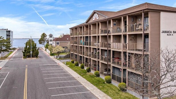 A multi-story hotel with balconies, a parking lot, and a view of the water. - Cozy Beach Escape (Ocean City)