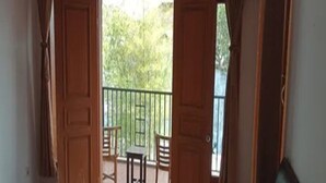 Una habitación con cama, una mesita y sillas en un balcón con vistas a zonas verdes.