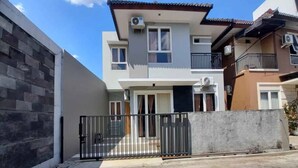 Edificio residencial de dos pisos con entrada porticada, balcón en el piso superior y camino de entrada pavimentado.
