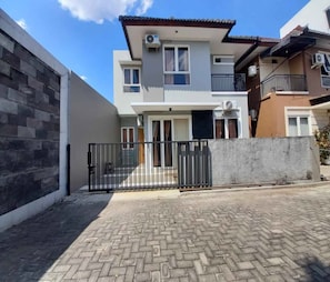 A two-story residential building with a gated entrance, a balcony on the upper floor, and a paved driveway. - Cozzy AV Home (Semarang)