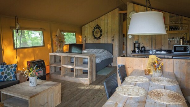 Een gezellige kamer met een bed, een eettafel met geweven tafelmatjes, een bank en een houten wand met een decoratieve spiegel.