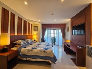 Camera d'albergo con un letto grande, una scrivania, una sedia, una televisione e un balcone con tende.