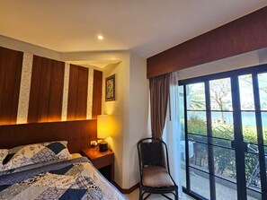 A hotel room with a bed, a chair, a nightstand, a lamp, and a large window with a view. - (Choeng Thale)
