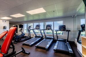 Ein Fitnessstudio mit Laufbändern, einem roten Trainingsstuhl und einem Ergometer.