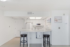 Eine moderne Küche mit einer zentralen Kochinsel, zwei Barhocker, einer Mikrowelle und einem Kühlschrank.