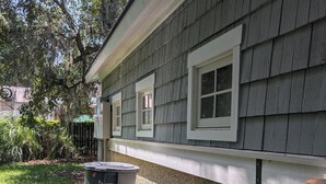 A house with a grey siding exterior, a white window trim, a green hose, and a trash can. - Canoe Club Studio - Bring you boat! dock slip available (Daufuskie Island)