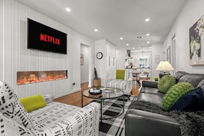A modern living room with a fireplace, a flat-screen TV, and a dining area in the background. - Bottles & Boots on Burbank - Hot Tub & Fireplace (Fredericksburg)
