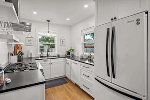 A modern kitchen with white cabinetry, a stainless steel refrigerator, and a gas stove. - Bottles & Boots on Burbank - Hot Tub & Fireplace (Fredericksburg)