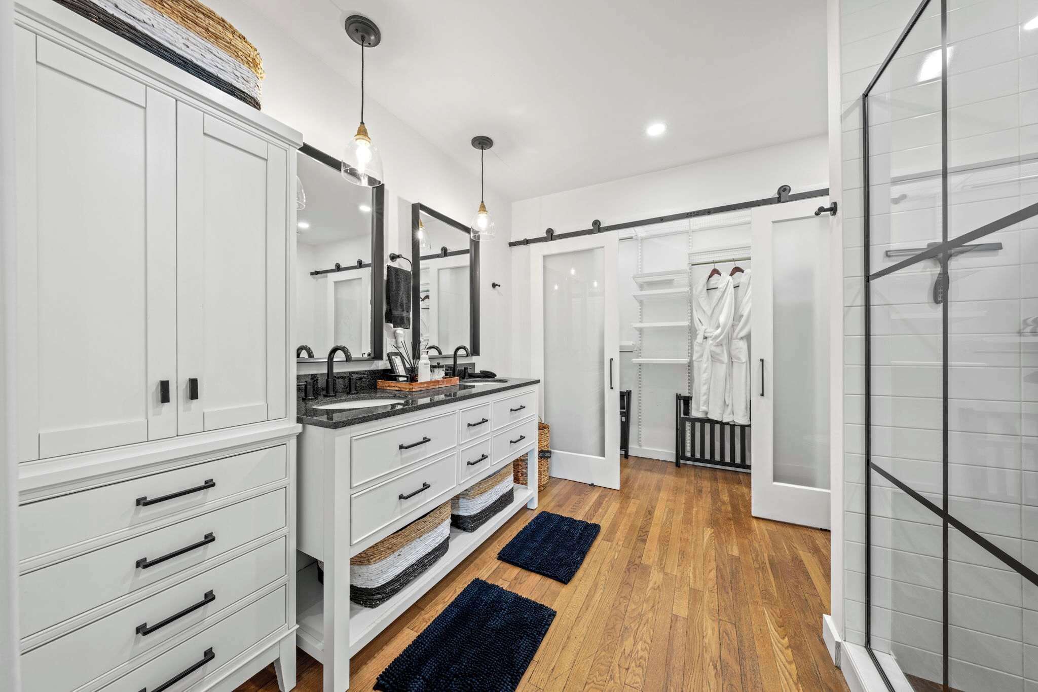 Un baño moderno con muebles blancos, tocador doble, cabina de ducha de vidrio y vestidor.