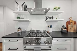 A kitchen with a stainless steel stove, white cabinetry, and decorative items on shelves. - Bottles & Boots on Burbank - Hot Tub & Fireplace (Fredericksburg)