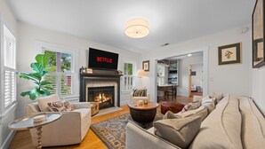 A living room with a fireplace, sofa, armchair, coffee table, and a TV displaying 'NETFLIX'. - Perla's Place - Fire Place & 3 Blocks from Main (Fredericksburg)
