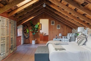 An attic bedroom with a wooden ceiling, a bed, a small table, a chair, and a potted plant. - Nimitz Loft - 1855 Historic Loft on Main St! (Fredericksburg)