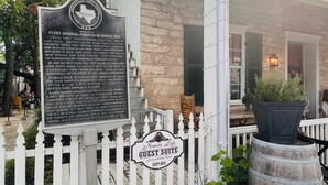 Um edifício histórico com uma placa que detalha sua importância, cerca branca de piquete e uma placa indicando a suíte de hóspedes.
