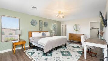 A bedroom with a bed, bedside table, dresser, desk, chair, and a ceiling light fixture.