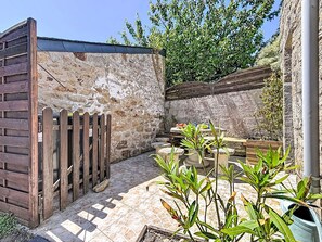 Ein Innenhof mit Steinmauern, einem Holenzaun, gefliestem Boden und Kübelpflanzen.