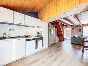 Eine moderne Küche mit weißen Schränken, einem Geschirrspüler und einem Spülbecken. Eine Treppe führt zu einem Erkerbereich mit Holzboden.