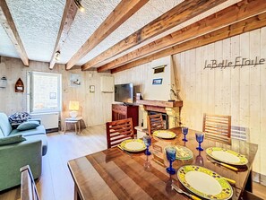Ein gemütlicher Essbereich mit einem Holztisch, gedeckt für vier Personen, einem Fernseher und einem Kamin.