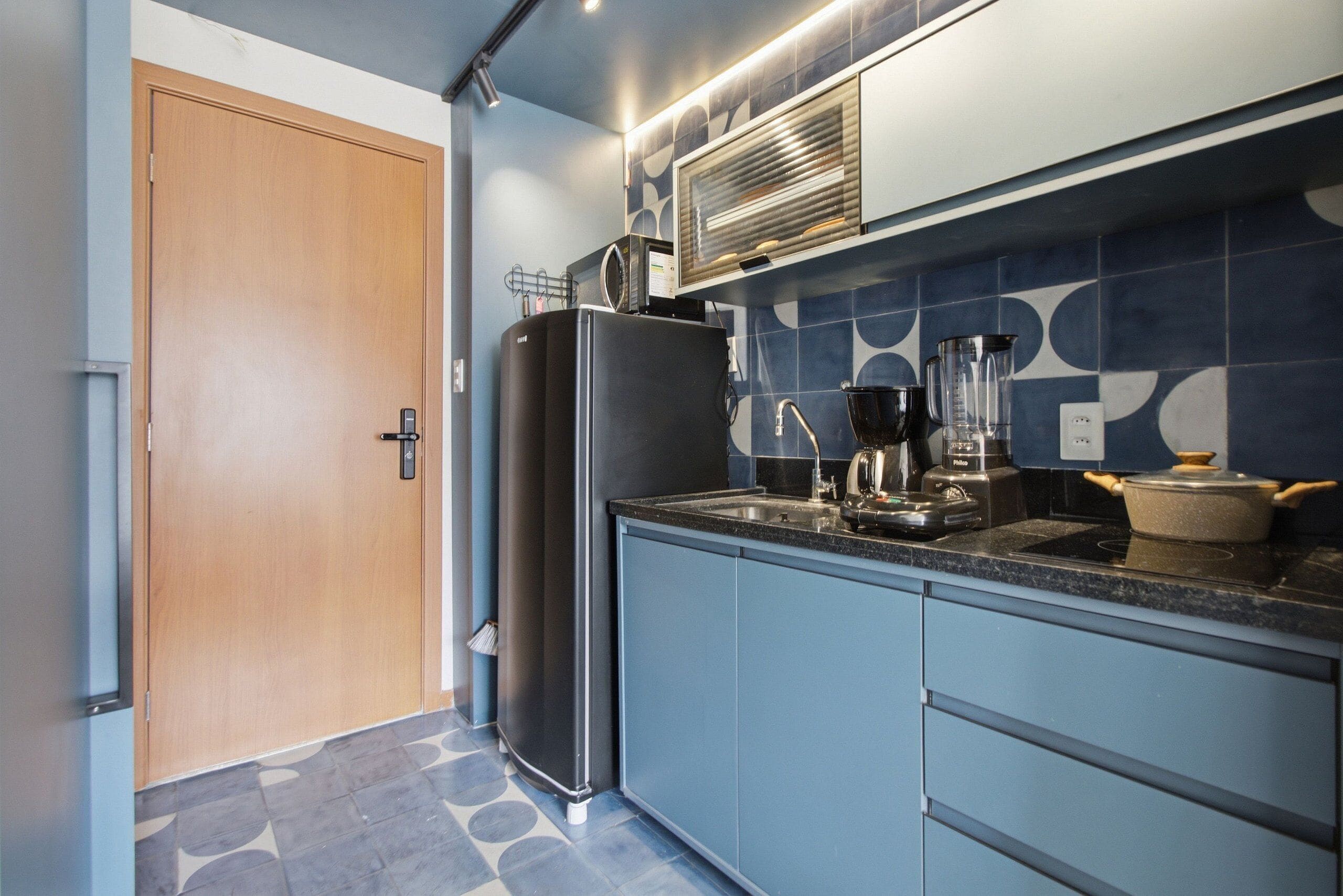 Une cuisine moderne équipée d’un réfrigérateur, d’un four à micro-ondes et d’une cuisinière, avec des armoires bleues et des carreaux décoratifs.
