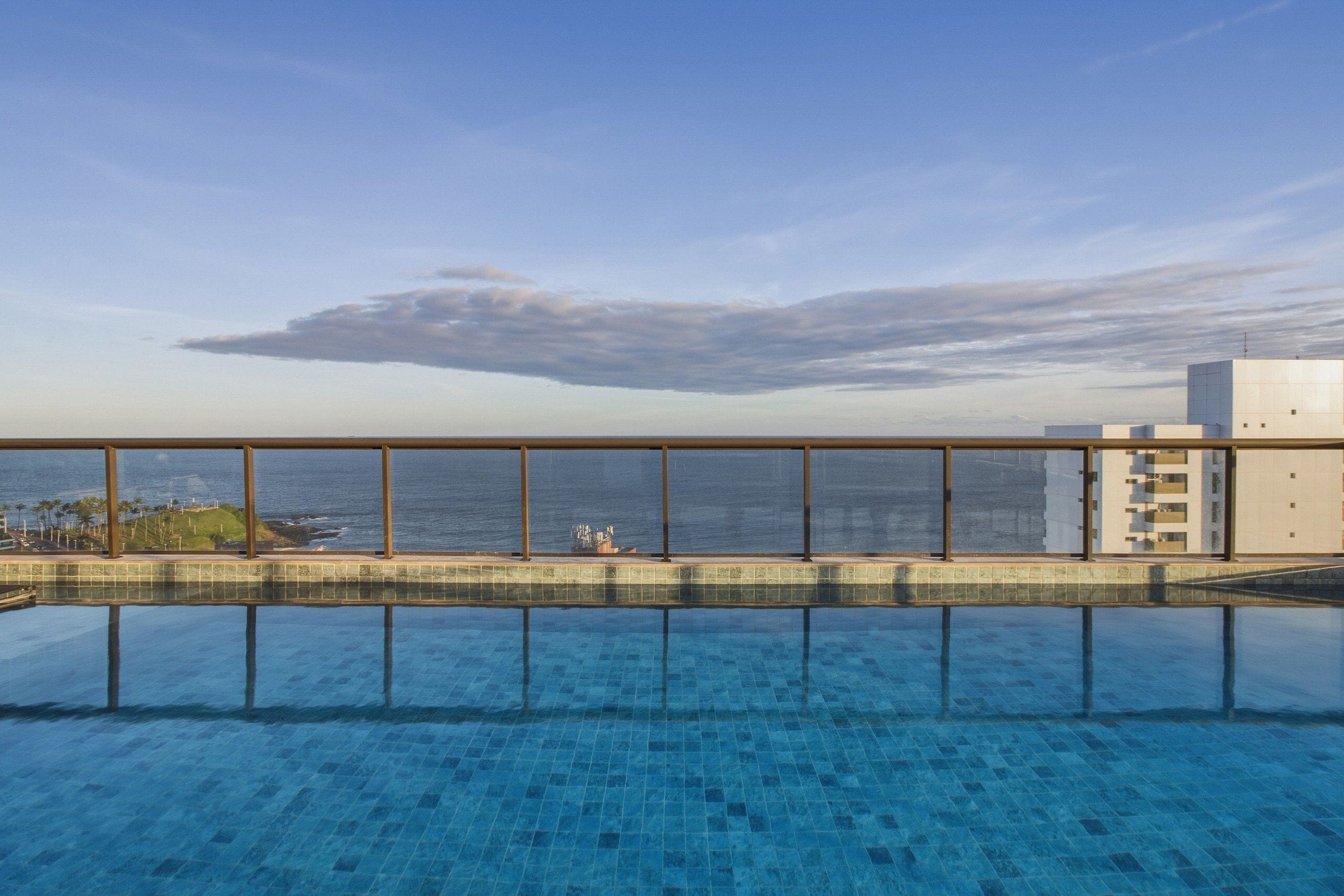 A clear view of a swimming pool with a glass barrier, a distant view of the ocean, and a clear sky.